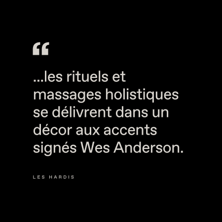 Le texte sur fond noir se lit comme suit : "...les rituels et massages holistiques se délivrent dans un décor aux accents signés Wes Anderson." Attribution : Les Hardis.