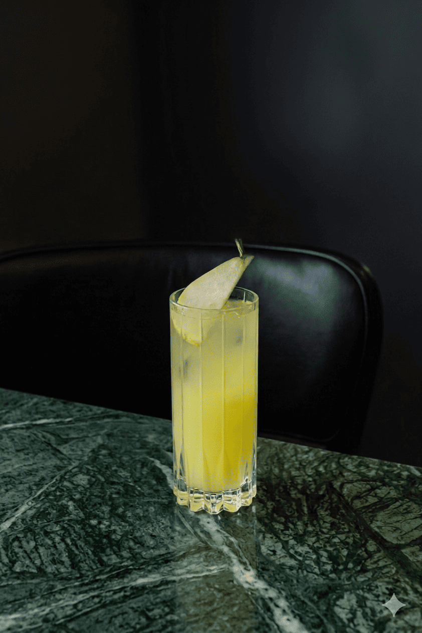 A tall glass of yellow drink with ice and a pear slice garnish sits on a green marble table, with a dark, blurred chair and background.